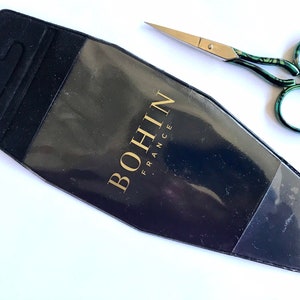 May include: A black and clear plastic case with a gold label that reads "BOHIN FRANCE". A pair of green and silver scissors with a decorative pattern are next to the case.