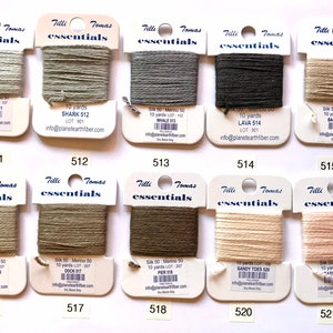 May include: Ten skeins of 10-yard silk and merino blend embroidery floss in various shades of beige, brown, and gray. Each skein is labeled with the color name, lot number, and website information. The skeins are arranged in two rows of five.