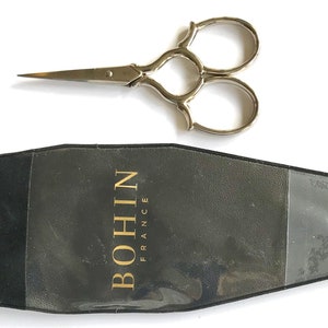 May include: Silver-toned embroidery scissors with three rings, in a black plastic case with the text "BOHIN FRANCE" printed in gold.