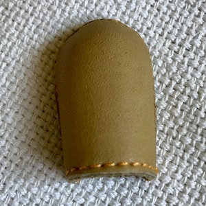 May include: A beige leather thimble with a gold stitching detail.