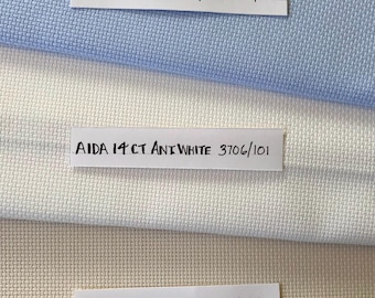 May include: Three Aida fabric swatches in different colors: light blue, white, and ivory. Each swatch has a label with the text "AIDA 14CT" and the color name and corresponding product code.