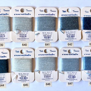 May include: Ten skeins of Tilli Tomas Essentials silk merino yarn in various shades of blue and grey. Each skein is labeled with the yarn name, color number, and yardage. The yarn is 50/50 silk and merino wool.