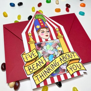 May include: A red and white striped card with a cartoon character peeking out of a window. The card says "I've bean thinking about you" and has a window filled with jelly beans.