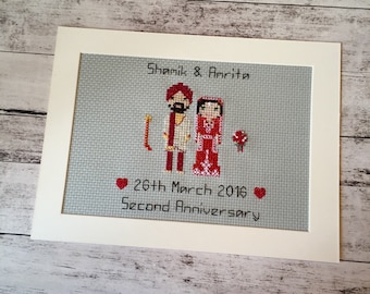 Pode incluir: Um bordado de ponto cruz emoldurado com um casal em roupas tradicionais indianas. O texto diz "Shamik & Amrita" e "26th March 2016 Second Anniversary".