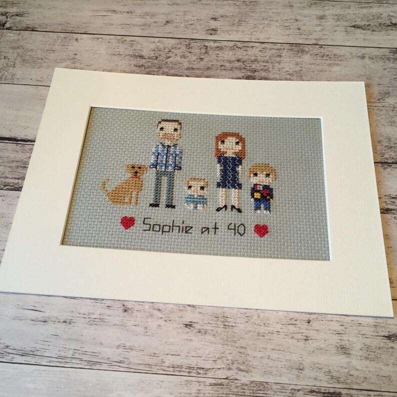 May include: A cross-stitch embroidery of a family with a dog. The family includes a man, a woman, a boy, and a baby. The embroidery is framed and has the text "Sophie at 40" with two red hearts.