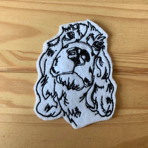 Puede incluir: Imagen bordada en blanco y negro de la cabeza de un perro sobre un fondo de fieltro blanco.
