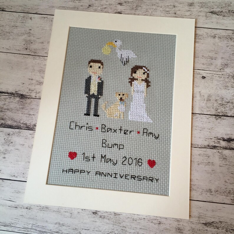 May include: A framed cross-stitch design featuring a couple, a dog, and a stork carrying a baby. The text reads "Chris Baxter Amy Bump 1st May 2016 Happy Anniversary".