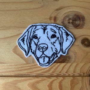 May include: White embroidered patch of a dog's head with black stitching. The dog has floppy ears, a long snout, and a happy expression.