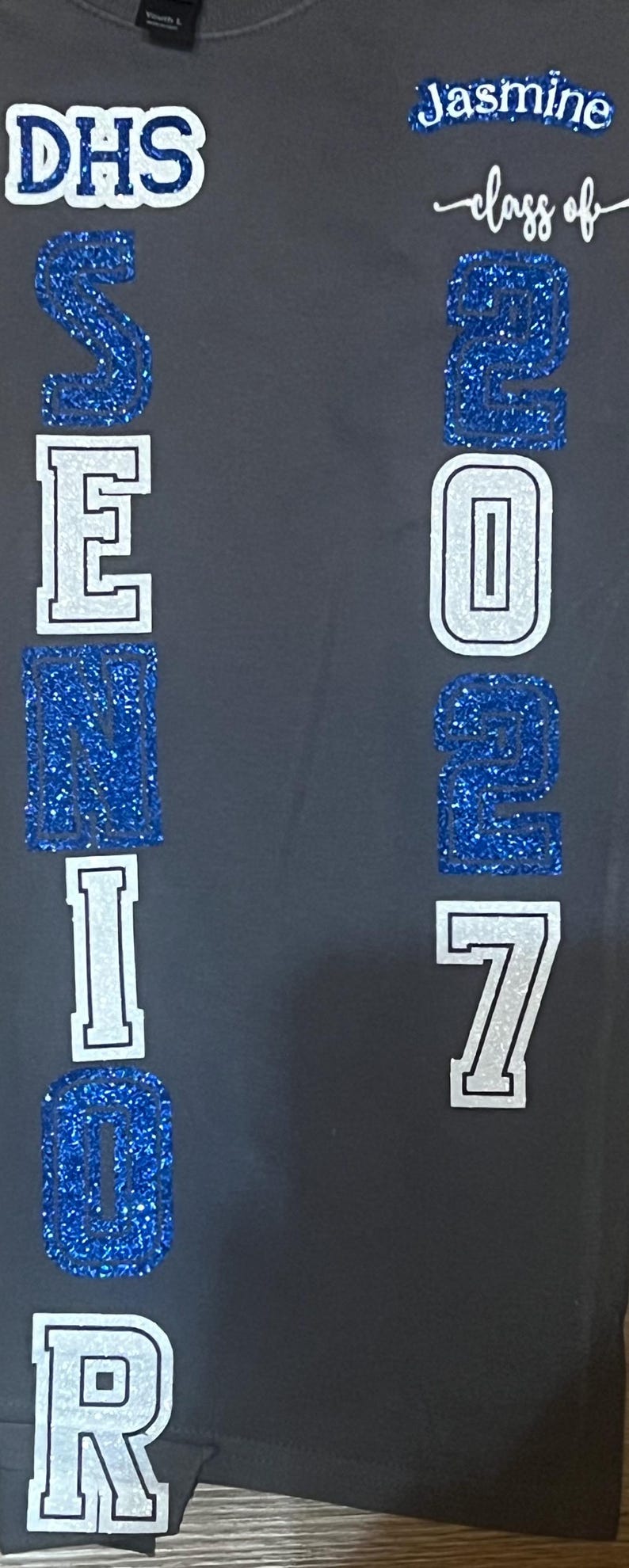 text "DHS SENIOR" in a combination of white and blue glitter lettering. The name "Jasmine" and "class of 2027" are also displayed in white glitter and blue glitter.