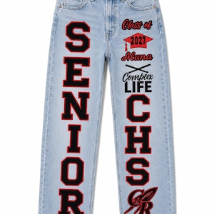 May include: Light blue denim jeans featuring the word SENIOR in large black and red block letters on the left leg. The right leg displays Class of 2027, a graduation cap, the name Alana, crossed batons, Complex LIFE, CHS, and a red and black logo.