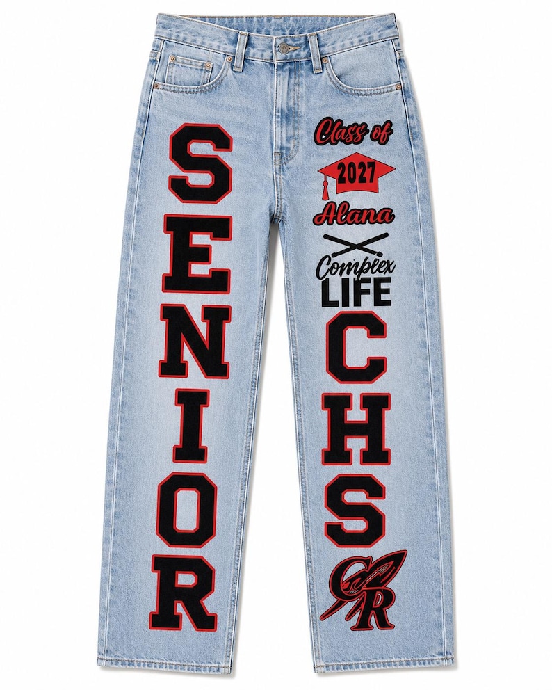 May include: Light blue denim jeans featuring the word SENIOR in large black and red block letters on the left leg. The right leg displays Class of 2027, a graduation cap, the name Alana, crossed batons, Complex LIFE, CHS, and a red and black logo.
