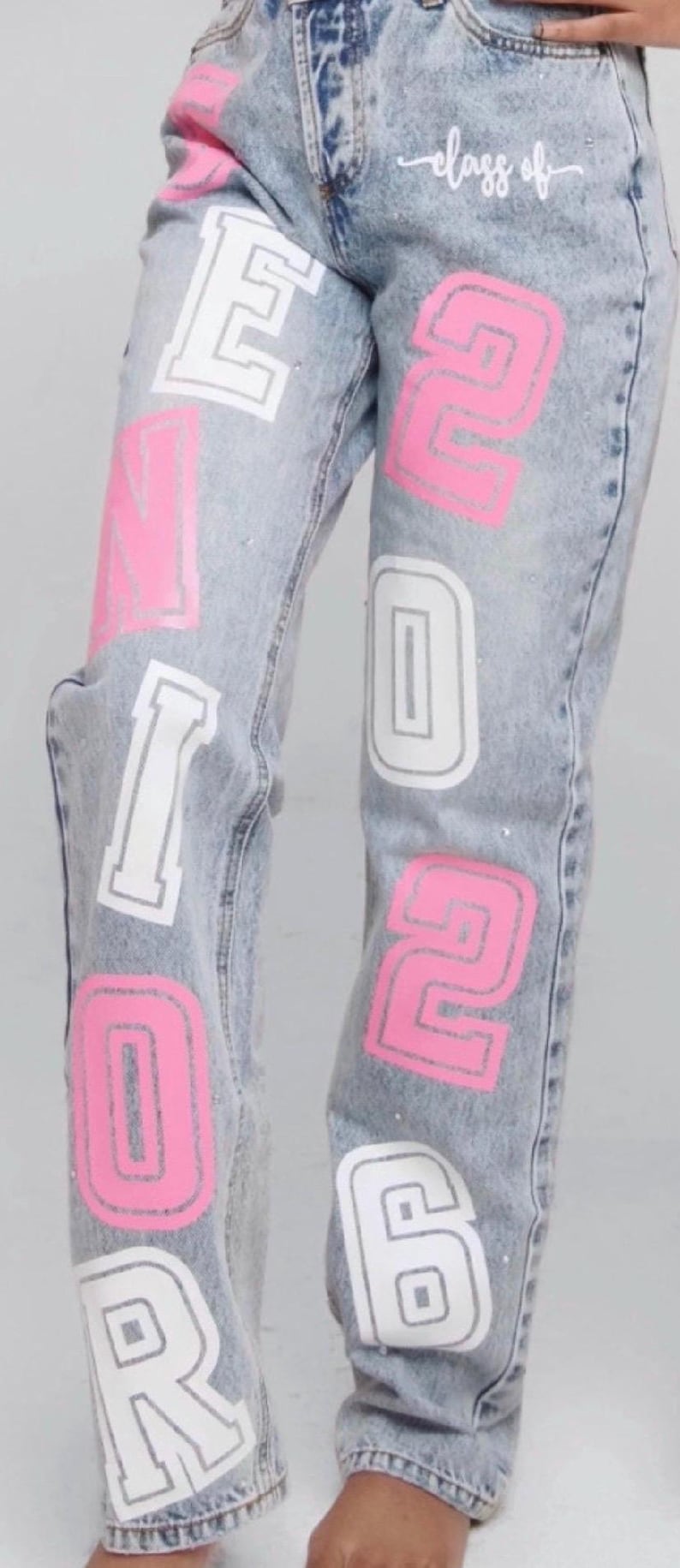 pink and white lettering spelling "SENIOR 2026" on the legs. The words "class of" are written in cursive ( this is what comes with this order if you order it regularly without personalization) two colors there is an upcharge for glitter as well as any personalization it is five dollars for each personal item such as name, school, initials, school logo, pom-pom, etc