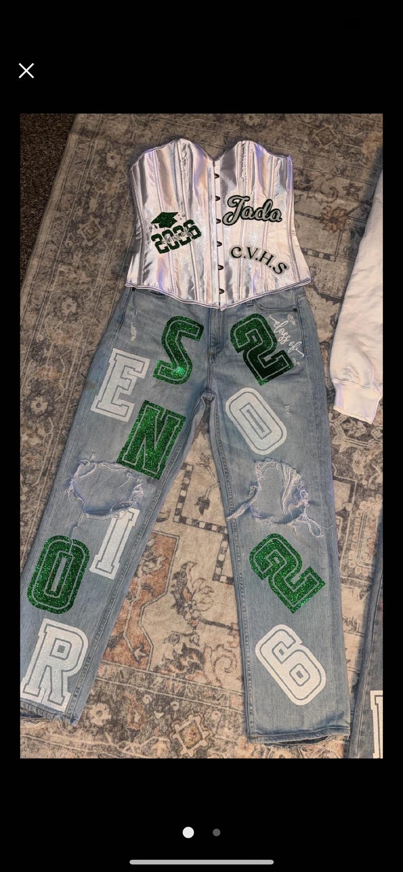 May include: A silver corset top and light wash denim jeans with distressed details. The jeans feature green and white lettering and numbers, including "2026" and "CVHS". A graduation cap graphic is also visible.