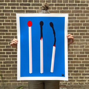 May include: A poster with a blue background features three large matchsticks. The first match has a red head, the second is burnt black, and the third is partially burnt. The matchsticks are white with pink accents.