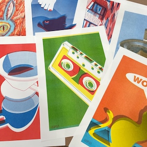 May include: A selection of vibrant art prints with diverse graphic designs. One print displays a yellow cassette tape on a green backdrop. Other prints feature a coffee maker, a building, and a cartoon animal. The word "OOPS!" is printed on some of the prints.