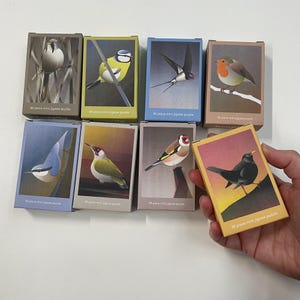 Könnte beinhalten: Ein Set mit neun Mini-Puzzles mit bunten Illustrationen verschiedener Vögel. Jedes Puzzle besteht aus 99 Teilen und wird in einer kleinen Schachtel mit einer Vogel-Illustration auf der Vorderseite geliefert.
