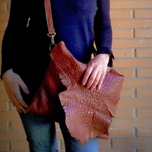 Pu&ograve; includere: Una donna indossa un maglione blu scuro a collo alto e jeans blu con una borsa a tracolla in pelle marrone con una patta testurizzata.