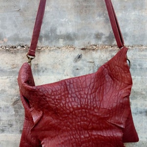 Pu&ograve; includere: Una borsa a tracolla in pelle rossa con una superficie strutturata. La borsa ha una tracolla lunga e una chiusura a lembo.