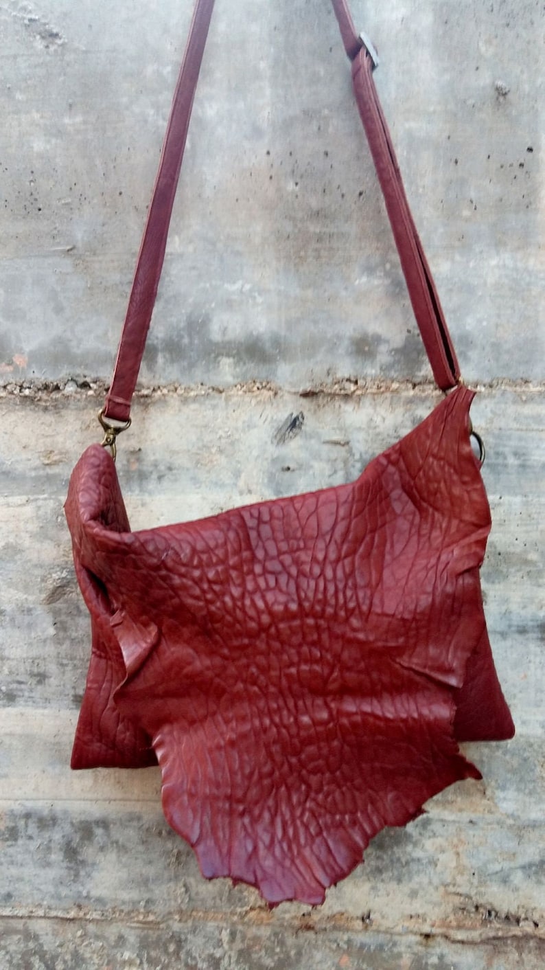 Pu&ograve; includere: Una borsa a tracolla in pelle rossa con una superficie strutturata. La borsa ha una tracolla lunga e una chiusura a lembo.