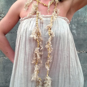 Puede incluir: Una mujer con un vestido blanco de lino y un collar largo y de capas hecho de tela beige y marrón y cuentas.