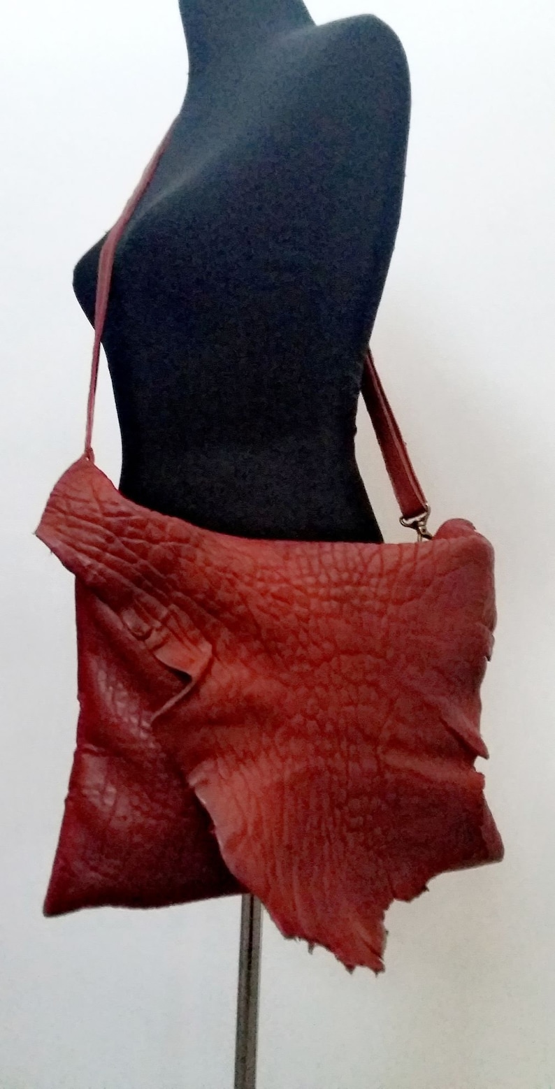 Pu&ograve; includere: Una borsa a tracolla in pelle rossa con una superficie strutturata. La borsa ha una lunga tracolla e una chiusura a lembo.