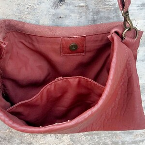 Pu&ograve; includere: Una borsa a tracolla in pelle rossa con chiusura a lembo e una tasca interna. La borsa ha una chiusura in ottone e una tracolla lunga.