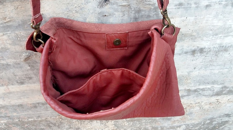 Pu&ograve; includere: Una borsa a tracolla in pelle rossa con chiusura a lembo e una tasca interna. La borsa ha una chiusura in ottone e una tracolla lunga.