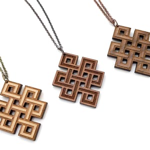 Puede incluir: Tres collares de madera con intrincados diseños de nudos. Cada collar presenta un colgante cuadrado con un patrón detallado e entrelazado. Los collares están sobre un fondo blanco.