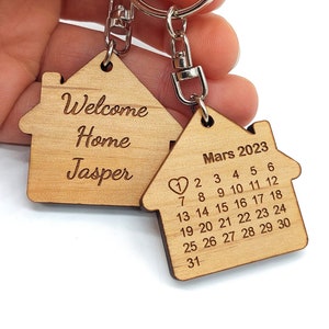 Peut inclure: Porte-clés en bois en forme de maison avec le texte "Welcome Home Jasper" d'un côté et un calendrier pour mars 2023 de l'autre.