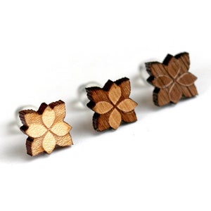 Puede incluir: Tres pendientes de madera con diseño de flor. Los pendientes son de diferentes tonos de marrón.