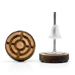 May include: A pair of wooden earrings with a circular design featuring concentric circles. The earrings are brown with a lighter brown centre and have silver posts.