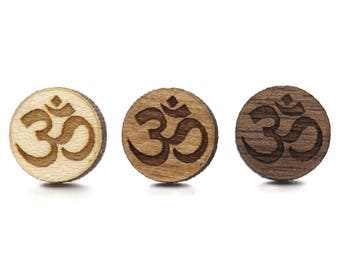 May include: Three wooden round ornaments with the Om symbol engraved in the center. The ornaments are in different shades of brown.