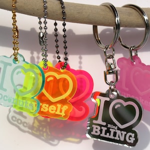 Puede incluir: Un conjunto de seis llaveros con diferentes dijes de acrílico de colores. Cada dije presenta un corazón con el texto "Me encanta" y una palabra diferente. Las palabras son "Coconut", "Myself", "Bling", "Cupcakes", "You" y "Life".