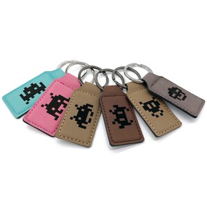 May include: Six keychains with different coloured leather and a pixelated alien design. The keychains are attached to silver key rings.