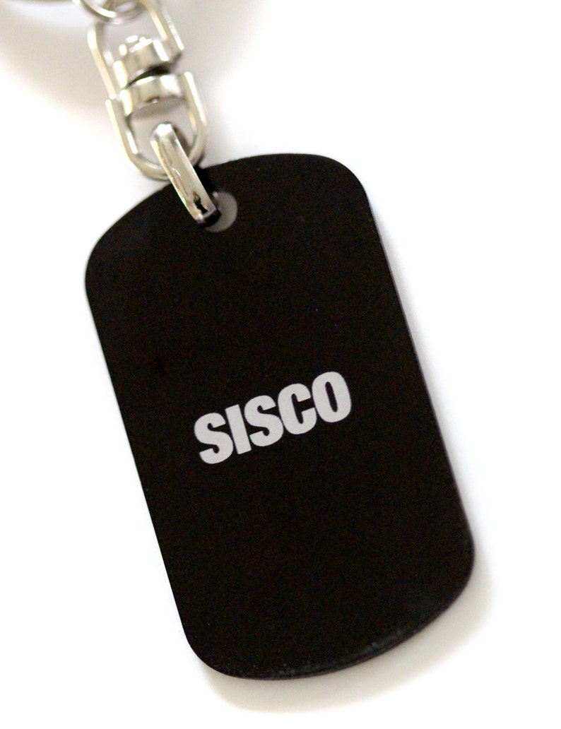 Puede incluir: Llavero de metal negro con un anillo plateado y una cadena plateada. La etiqueta tiene la palabra "SISCO" impresa en blanco.