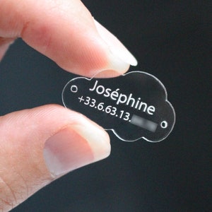 Può includere: Un'etichetta di plastica trasparente a forma di nuvola con il nome "Joséphine" e un numero di telefono +33.6.63.13. seguito da una serie di numeri.