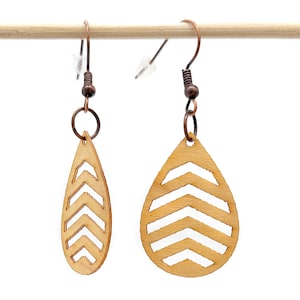 Può includere: Un paio di orecchini in legno con un motivo a chevron. Gli orecchini hanno la forma di una lacrima e hanno un gancio color rame.