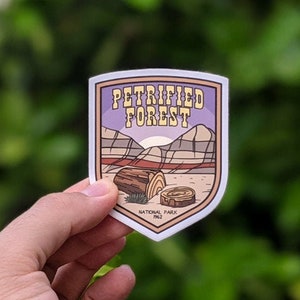 May include: A purple and yellow sticker with a cartoon illustration of a petrified log and the text "Petrified Forest National Park 1962".