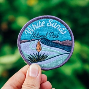 May include: A blue and white embroidered patch with the text "White Sands National Park" and a stylized image of a desert plant.