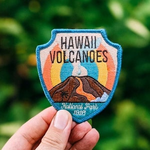Könnte beinhalten: Ein blauer und orangefarbener gestickter Aufnäher mit dem Text "Hawaii Volcanoes National Park 1916". Der Aufnäher zeigt ein stilisiertes Bild eines Vulkans mit einer Rauchwolke.