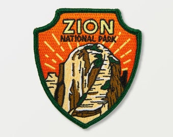May include: Embroidered patch featuring the words "ZION NATIONAL PARK" above a mountain illustration. The patch has an orange background with yellow sun rays, a green border, and is shield-shaped.