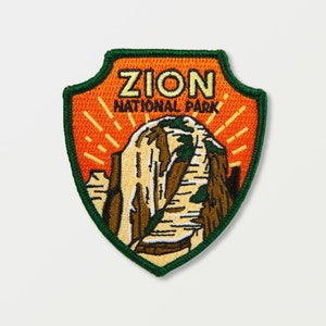 Pode incluir: Um remendo bordado laranja e verde com o texto "Zion National Park" e uma representação de uma cordilheira.