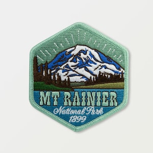Puede incluir: Un parche bordado hexagonal verde con una imagen azul y blanca del Monte Rainier y el texto "MT RAINIER National Park 1899".