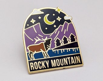 May include: Gold enamel pin with a night scene of mountains, a crescent moon, stars, and a deer. The text "ROCKY MOUNTAIN" is at the bottom of the pin.