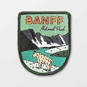 May include: Embroidered patch featuring the text "BANFF National Park" in orange letters. The patch depicts a mountain goat, mountains, and a lake. The patch has a green border and a light green background.