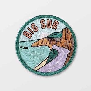 May include: A green, round embroidered patch with the words "BIG SUR" in orange lettering. The patch features a scenic view of a winding road along a coastline with a bridge and cliffs.