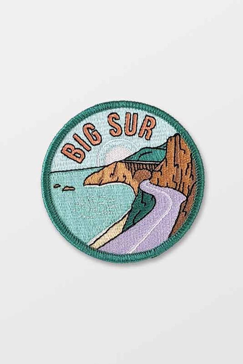 K&ouml;nnte beinhalten: Gestickter Aufn&auml;her mit einem Big Sur-Design. Der Aufn&auml;her zeigt eine K&uuml;stenlandschaft mit einer Stra&szlig;e, einer Br&uuml;cke und dem Ozean. Der Text "BIG SUR" ist oben aufgebogen. Der Aufn&auml;her hat einen tealfarbenen Rand und einen hellblauen Hintergrund.