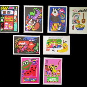 May include: A collection of eight colorful prints featuring various illustrations and text. The prints are framed in black and feature a variety of themes, including food, animals, and abstract designs. The text on the prints includes "Pocket Pal Pencil Sha", "Bubble Yum", "Hillo", "Asahi", "Noma", and "Bite O' Honey".