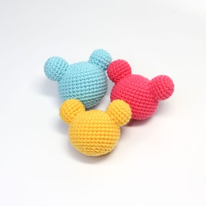 以下が含まれることがあります： 大きな耳を持つクマの形をした、かぎ針編みで作ったぬいぐるみが3つあります。クマは青、ピンク、黄色です。