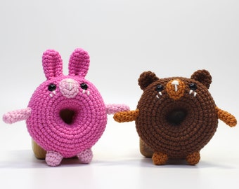 Op de afbeelding: Twee gehaakte donutvormige knuffels, een roze met konijnenoren en de andere bruin met berenoren.